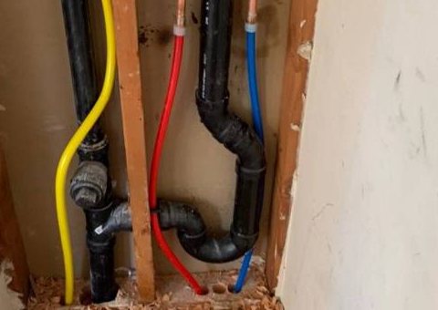 Black drain pipe and trap inside an open wall, next to red and blue water lines